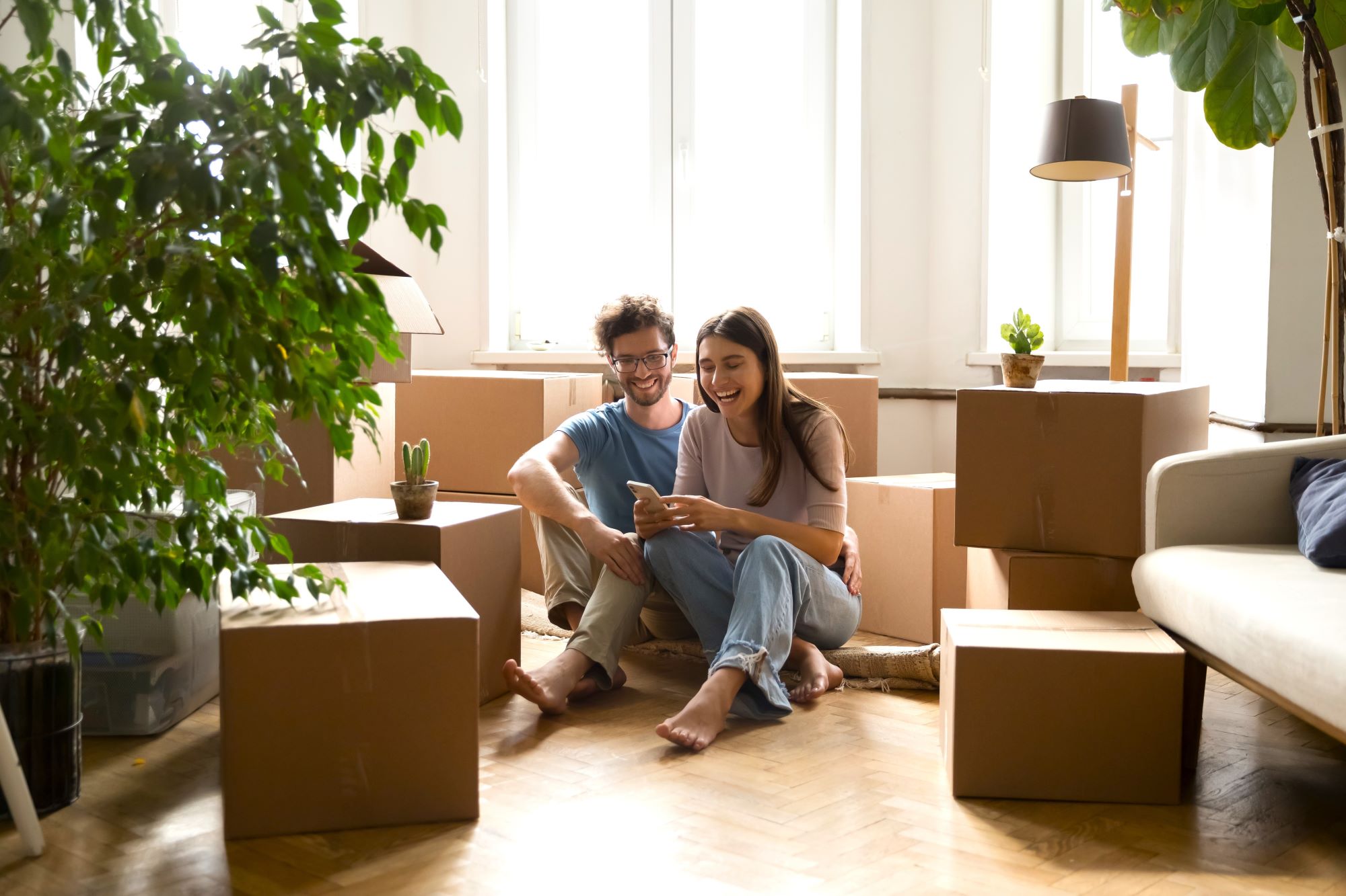 Happy young couple sitting in an apartment surrounded by their boxed belongings.